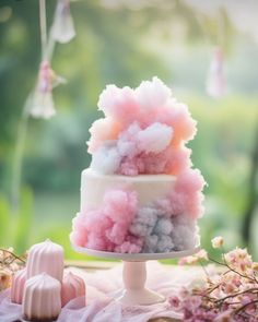 a cake with pink and blue frosting on top sitting on a table next to flowers