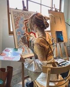 a woman sitting in front of an easel painting