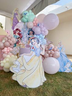 there are many balloons and princesses on the grass in front of this cake stand