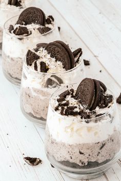 three desserts with oreo cookies and whipped cream in small glass dishes on a white wooden table