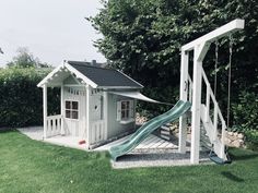 a small white house with a slide in the yard