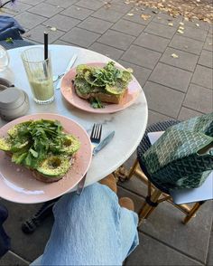 two plates with avocado toast on them and a glass of water next to it