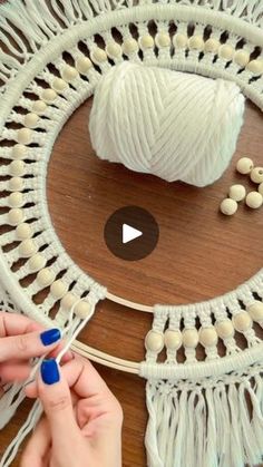 someone is knitting yarn on a wooden table with white balls and needles in front of it