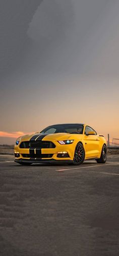 a yellow mustang parked in an empty parking lot at sunset with the sun setting behind it