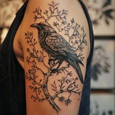 a black bird sitting on top of a tree branch with leaves and branches around it