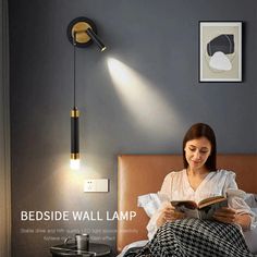 a woman sitting in bed reading a book under a wall light that is turned on