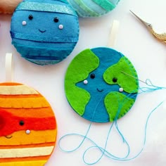 three ornaments made to look like planets on a white table with scissors and thread spools