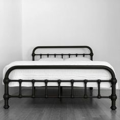 a black and white photo of a bed in a room with wood flooring on the ground