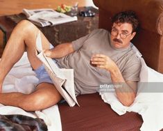 a man laying on top of a bed reading a paper while holding a glass in his hand