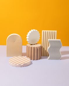 three wooden sculptures sitting next to each other on a white table top with an orange wall in the background