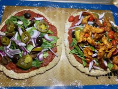 two pizzas sitting on top of a wooden cutting board covered in sauce and veggies