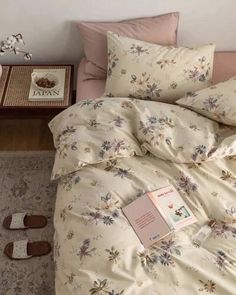 a bed with floral sheets and pillows on top of it next to a small table