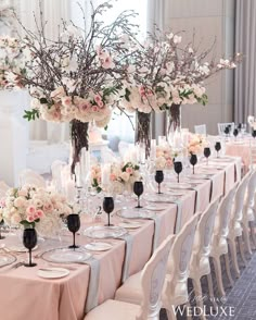 the table is set up with white and pink flowers in vases, candles and wine glasses