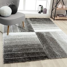 a living room area with a chair and rugs on the floor, in front of a window