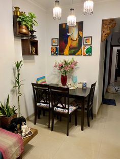 a dining room table and chairs with paintings on the wall behind them, in front of a couch