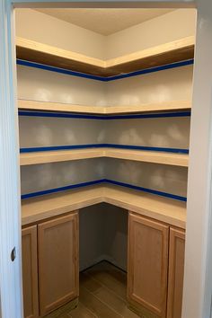 an empty pantry with wooden cabinets and blue tape on the shelves in it's corner