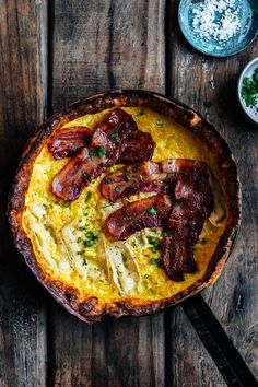 an omelet with bacon and cheese in a skillet on a wooden table