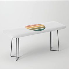 a white bench with a rainbow design on the top and black metal legs, sitting in front of a white background