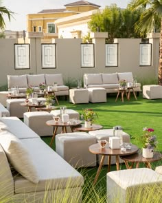 an outdoor seating area with white couches, tables and flowers on the grass in front of a building