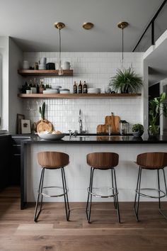 two bar stools sitting in front of a kitchen counter with plants on the shelves