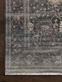 an area rug with flowers and leaves on the side, in dark grey tones against a wooden background