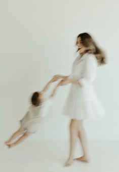 a woman holding the hand of a small child in front of a white wall with her legs spread out