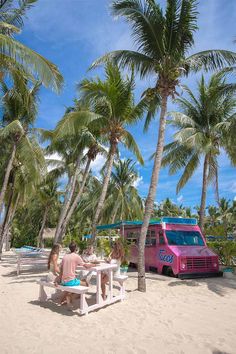 two people sitting at a picnic table on the beach with a pink van in the background