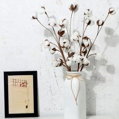 a white vase filled with cotton sitting on top of a table next to a framed photograph