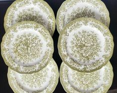 four antique china plates with gold and white floral designs on them, all stacked together