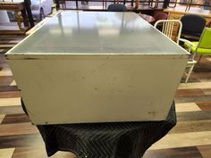 an old white refrigerator sitting on top of a wooden table in a room with chairs