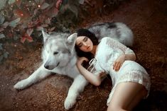 a woman laying on the ground next to a wolf with her head resting on her chest