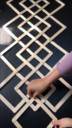 a person is making a geometric pattern out of popsicle sticks and plywood strips