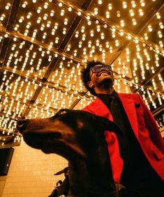 a man in a red jacket and black tie standing next to a dog with his eyes closed