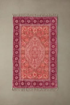 a pink and red rug with fringes hanging on a wall next to a gray wall