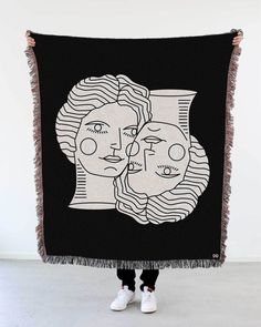 a woman holding up a red and white tapestry with two women's faces on it