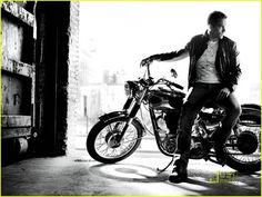 a man sitting on top of a motorcycle next to a brick building and another bike behind him