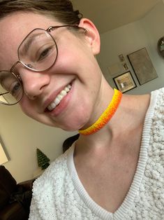 a smiling woman wearing glasses and a yellow necklace with an orange bead around her neck