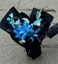 a bouquet of blue flowers sitting on top of a black piece of paper in someone's hand