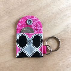 a pink and black cell phone case sitting on top of a wooden table next to a metal keychain