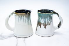 two white and blue mugs sitting next to each other on a marble counter top