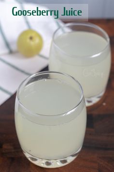 two glasses filled with white liquid sitting on top of a wooden table next to an apple