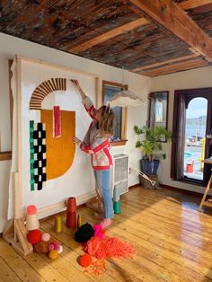 a woman is painting on the wall in her living room with colorful yarn and wood