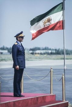 a man in uniform standing next to a flag on top of a red platform near the water