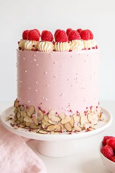 a pink cake with raspberries and almonds on top, sitting on a white plate