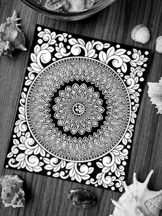 a black and white photo of an intricately designed doily on a table next to seashells