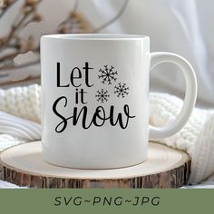 a white coffee mug with the words let it snow on it sitting on top of a tree stump