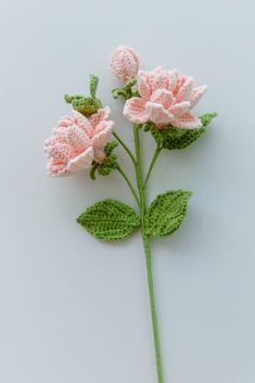 two crocheted pink flowers with green leaves on a white surface, ready to be made into an ornament