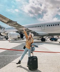 a woman standing in front of an airplane with her hand up and luggage on the ground