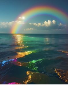 a rainbow in the sky over water with clouds and sun reflecting off it's surface