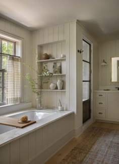 a bath tub sitting under a window next to a wooden shelf filled with vases